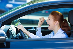 Closeup portrait displeased angry pissed off aggressive woman driving car, shouting at someone, fist hand up in air isolated traffic background. Emotional intelligence concept. Negative human emotion